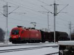 1116 089-4 durchfährt bei Schneetreiben mit einem Güterzug den Bhf.