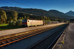 Angestrahlt von der Abendsonne, donnert 1144 018-9, mit einem Mischer in Richtung Villach, durch den Bahnhof Greifenburg-Weißensee.