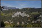 Panoramabild der Semmeringbahn mit Kalter Rinne , Poleroswand und Krauselklause. Die Berge im Hintergrund sind die Rax und der Schneeberg. Der Lokzug der auf dem Krauselklauseviadukt fährt, findet wegen seiner Winzigkeit kaum Beachtung.