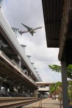 Unten der Bf. Lat Krabang, darüber die gleichnamige Haltestelle des SRTET-Airport Link und ganz oben die Thai Airways Boeing 777-3D7, Kennzeichen HS-TKE beim Anflug auf den Suvarnabhumi Airport. Bild vom 10. März 2012.