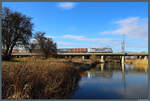 386 003 der Metrans Rail spiegelt sich im Wasser der Ehle, als sie sich am 01.03.2026 mit einem Containerzug Biederitz nähert.