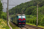Elektrolokomotive TschS7-121 mit einem internationalen Zug von Budapest nach Kiew rauscht im Regen / Volovets, Ukraine / 09.07.2025