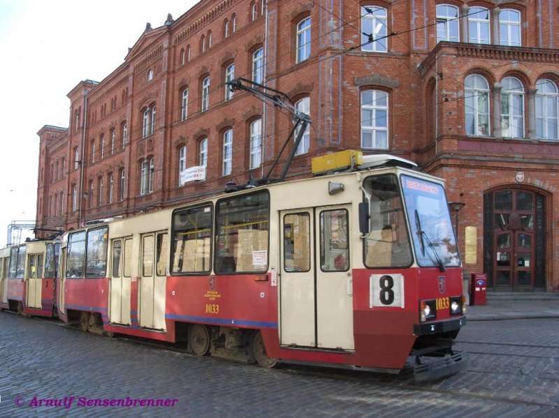 Tram 1033 unterwegs auf Linie 8 vor der Hauptpost.

Die hier eingesetzten polnischen Standardtrams vom Typ Konstal 105Na unterscheiden sich gern in Details: Der rotlackierte 1033 hat einen Einholmbgel, eine Klimanalage fr die Fahrerkabine, einen Lautsprecher auen ber der ersten Tr, sowie eine Matrixzugzielanzeige. Er besitzt ltere Klapptren mit je einem Fenster.  Die Linienstecknummer befindet sich an der Seite.

06.04.2007 Szczecin (Stettin)