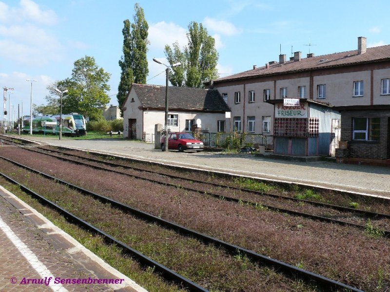 Turmbahnhof Kostrzyn (Kstrin-Neustadt): Bahnsteig 1 -oben- mit zweisprachig beworbener Friseurwellblechbude. Trotz potentieller Kundschaft hatte diese allerdings Samstags geschlossen.
Hinten steht Triebzug SA133-008 der Wojewodschaft Lebus = Wojewdztwo lubuskie.
