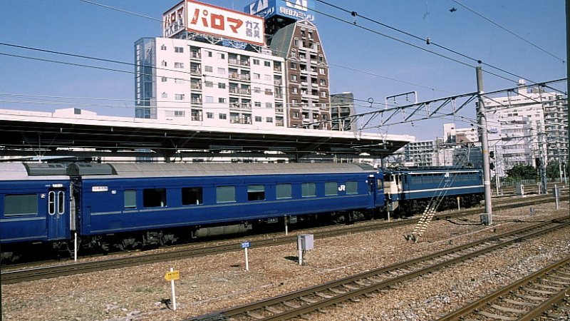 Typ 25 Schlafwagen. Bis auf einzelne Sonderzüge wird 100% des Personenverkehrs in Japan mit Triebwagen gefahren; Ausnahme sind ganz wenige verbleibende Schlafwagenzüge. Typ 25 wurde 1973-1980 gebaut; sie weisen 2 statt 3 Betten übereinander im Abteil auf.Im Januar 2008 wurden wieder 28 Wagen von 1067mm auf 1000mm-Spur umgespurt und nach Thailand abgegeben. Hier steht O-HA-NE-FU 25 27 (オハネフ25 27) in Shin Osaka, 14.März 1999. (O オ　＝　Personenwagen der Gewichtsklasse 32,5-37,5 t; HA ハ ＝Wagen der Normal(=nicht Luxus-)klasse; NE ネ　＝mit Betten; FU フ　＝mit Personalabteil)。