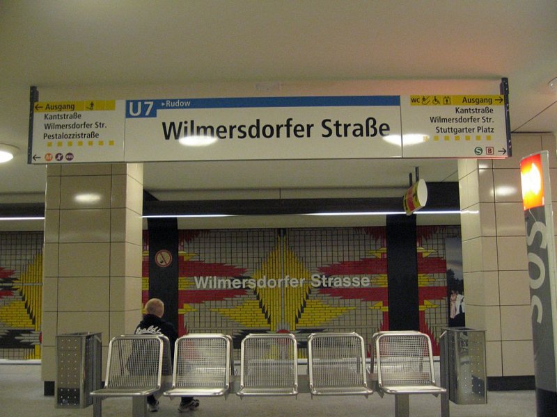 U-Bahnhof Wilmersdorfer Str.: Der von Rmmler 1978 gestaltete Bahnhof wurde mit einem bunten Mosaik aus Keramikplatten an den Wnden verziert, das das Wilmersdorfer Stadtwappen mit seiner Bourbonlilie darstellen soll. Der erst sehr dunkle Bahnhof wurde nun mit weissen Platten an den Sttzen aufgehellt, ebenso wurde der Bodenbelag ausgewechselt.
Ein bergang zur S-Bahn ist vorhanden, der aber ein paar Meter im Freien verluft.
