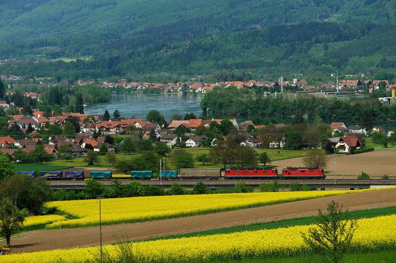 ber eine Autobahnbrcke fhrt der Gterzug mit einer Re 4 4 II und einer Re 6 6 vorbei an blhenden Rapsfeldern. Der Rhein dahinter teilt die beiden Orte Wallbach Aargau und Wallbach Baden-Wrttemberg im Hintergrund. 9.5.2008