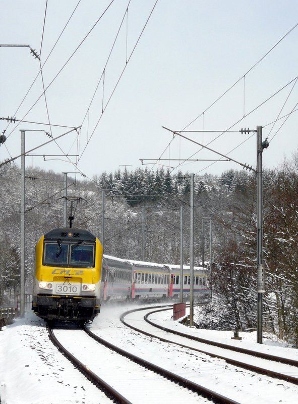 Um 11.08 am 25.03.08 hatte das Schneegestber aufgehrt und die Sonne zeigte sich sogar, als E-Lok 3010 mit ihren schneebedeckten Wagen aus Richtung Clervaux durch die Kurve vor Enscherange fhrt.