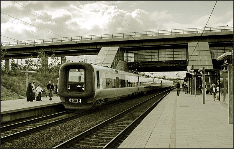 Umsteigebahnhof -

Station Ørestad im Süden von Kopenhagen an der Strecke zur Øresundbrücke. Über die Treppenaufgänge im Hintergrund kann zur Metrolinie M1 umgestiegen werden, die hier als Hochbahn die Bahnstrecke kreuzt. In den Bahnhof eingefahren ist soeben ein Øresund-Expresstriebzug (Mehrsystem) mit dem für die Triebwagen in Dänemark so typischen Gummiwulst an der Stirnseite. Die Führerhäuser können beim Zusammenkuppeln der Triebwagen zu Seite geschwenkt werden, um den Durchgang zwischen den Zügen zu ermöglichen. Wir empfanden die Züge als sehr komfortabel, anders als die Baureihe 425 in Deutschland. 

23.8.2006 (M)