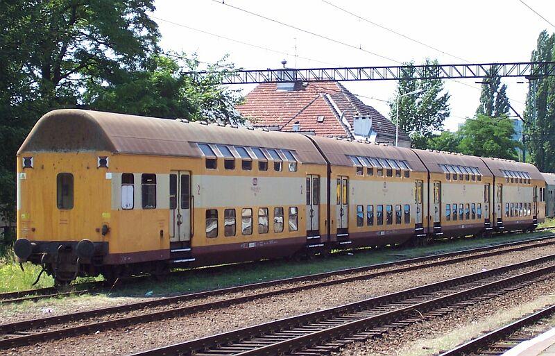 Vierteiliger Doppelstock-Gliederzug der PKP in gelb/hellgrau/rot am 25.06.2005 in Wroclaw Glowny (Breslau). Die Zge haben an den beiden Zugenden je ein zweiachsiges Drehgestell und zwischen den Wagen drei dreiachsige Jakobs-Drehgestelle, deswegen sind die Einheiten auch nicht trennbar.