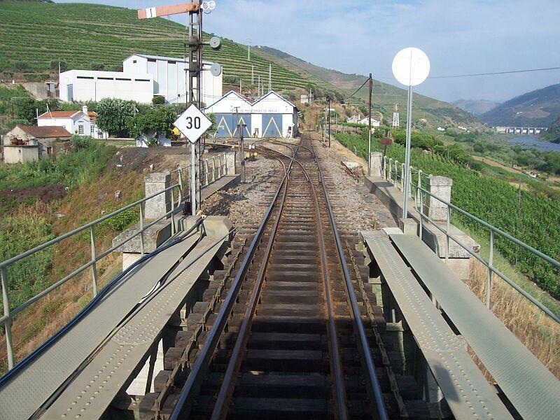 Vom Bahnhof Regua f�hrt etwa einen Kilometer ein 4-Schienen-Gleis, die Breitspurstrecke geht weiter durch das Douro-Tal nach Pocinho, rechts die 3.Schleuse mit 25 m Stauh�he, die Schmalspurstrecke f�hrt nach links in ein Seitental nach Vila Real. Das kleine BW an der Abzweigung hat beide Spurweiten und ein sch�nes Formsignal ist auch noch vorhanden.