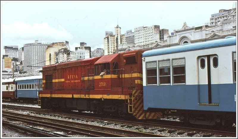 Vor der Silouette der Millionenstadt Belo Horizonte in Minas Gerais rangiert die schmalspurige RFFSA Lok 2708 Vorortswagen der S-Bahn nach Sabar. (Archiv 03/1979)