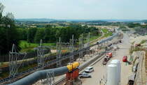 NBS Wendlingen - Ulm: Am 09.07.2017 bot sich dieser Blick von der Besuchertribüne am Tunnelmund des im Bau befindlichen Bosslertunnels bei Aichelberg. Der Tunnel wird 8.806 m der längste der Neubaustrecke sein. Links ist das Förderband zum Abtransport des Tunnelaushubs zu erkennen, in der Mitte die Be-/Entlüftung. Das in der Mitte sichtbare 900 mm-Gleis gehört zur Stollenbahn, die die Tübbinge (vorgefertigte Betonsegmente zur Tunnelversteifung) vom Lagerplatz zur Tunnelvortriebsmaschine transportiert. Auf dem Nebengleis ist ein Bauzug mit Lok L 2 (B-dh Schöma 5740/02 CHL350DCL) abgestellt.