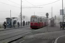 Wien Wiener Linien SL 6: Die Haltestelle Leberberg (XI, Simmering, Kaiserebersdorf) am Morgen des 16. Oktober. Eine E2+c5-Garnitur (E2 4093 und c5 1493) hält an der Haltestelle in Richtung Zinnergasse, während die Fahrgäste an der Haltestelle in Richtung Burggasse / Stadthalle noch einige Sekunden auf ihren Zug, dessen Stromabnehmer in Sicht ist, warten müssen.