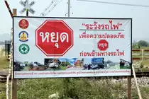 Auf diesem Plakat (gesehen am Bahnübergang der Strasse 1026 zwischen Sam Krathai und Kui Buri am 04.02.18) wird vor der Gefährlichkeit beim Überqueren auf höhengleichen Bahnübergängen mit Fotos von spektakulären Unfällen zwischen Autos und Zügen gewarnt. Obwohl alle Bahnübergänge, die ich gesehen habe, mit Lichtzeichen und Halbschranken ausgestattet sind, kommt es öfters zu Unfällen, weil entweder die Anlagen hin und wieder nicht funktionieren oder die Halbschranken einfach umfahren werden. Das rote Schild ist das thailändische Stop-Schild.  
