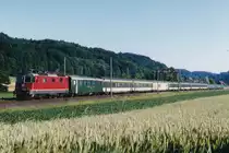 SBB: Re 4/4 II im Personenverkehr.
Schnellzug Genève-St. Gallen mit einer nicht erkennbaren Re 4/4 II der zweiten Serie bei Bollodingen unterwegs im Juli 1999.
Besondere Beachtung gilt nebst der bunten Anhängelast dem Gepäckwagen sowie dem Coop Shop-Wagen.
Foto: Walter Ruetsch 