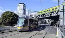Die Straßenbahn LUAS 3009 am Beresford Place unter der Hochbahn von DART. Auf der Brücke wird die Straßenbahn von einem Treibzug überquert. Aufnahme: 10. Mai 2018.