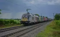 TXL 182 523 entflieht mit einer kalten BLS 486 und dem 42013, Wanne-Eickel Wst - Gallarate der Regenfront im Hintergrund. Aufgenommen am 30.05.2018 am Bahnsteigende des Haltepunkts Buggingen.