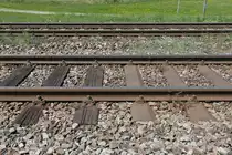 Zwei Gleise und drei unterschiedliche Arten von Schwellen. Hinten das Gleis in Fahrtrichtung Lindau mit Betonschwellen und vorne das Gleis aus Fahrtrichtung Lindau mit Holz- und Stahlschwellen. Der Gleisausschnitt der Allgäubahn wurde am 06.05.2018 bei Hergatz über einen Zaun fotografiert, der zwischen den Gleisen und einem Fußpfad steht.