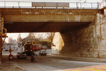 Nyon - Saint-Cergue - Morez NStCM.
Zur heutigen Zeit kaum mehr denkbar. Die damalige NStCM-Streckenführung als Strassenbahn zur Endhaltestelle Nyon. Ein Sportzug auf der Rückfahrt aus dem Jura beim Passieren der 1917 erbauten SBB Unterführung im Januar 1979. Besondere Beachtung gilt dem Skiwagen am Zugsschluss.
Die NStCM nimmt seit Juli 2004 in einem neu erbauten unterirdischen Kopfbahnhof in Nyon ihren Anfang.
Nahe der Haltestelle L'Asse findet das jährliche Paléo Festival statt.
Foto: Walter Ruetsch 