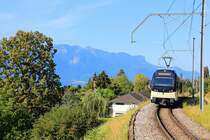 Die  Vororte  der Stadt Vevey müssen den Steilhang hinauf wachsen; dort werden sie von der MVC bedient. Im Vordergrund Triebwagen 7503 bei Château d'Hauteville; im Hintergrund die französischen Berge jenseits des Genfersees. 2.August 2018 