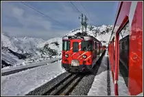 R823 kreuzt in Nätschen einen Autozug nach Sedrun mit einem Deh 4/4. Im Hintergrund ist das Urserental mit Hospental und Realp zu sehen. (16.04.2019)