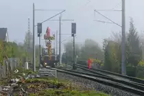 Bauarbeiten zur Elektrifizierung der Bodenseeg�rtelbahn, Streckenabschnitt Friedrichshafen - Lindau (||) - Herbstzeit = Nebelzeit am Bodensee. Mit Hilfe eines Mehrzweckarbeitsger�tes befestigen Monteure am 26.10.2019 im Bahnhof von Eriskirch den Fahrdraht am Tragseil.