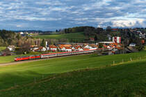 Das Fotografenglück für dieses Jahr habe ich bei diesem Bild vermutlich schon komplett ausgeschöpft. Am 11. Januar 2020 gab sich eine weitere Leihlok vor dem für eine kurze Periode wieder zwischen Lindau und Stuttgart in Verkehr gesetzten IC  Bodensee  die Ehre. Die orientrote 218 402 von Railsystems brachte den IC 119 gemeinsam mit der Ulmer 218 491 umleitungsbedingt über die Allgäubahn zu seinem Zwischenziel. Leider zeigte sich der Tag bewölkt und regnerisch. Trotzdem war ich im Westallgäu unterwegs, die freie Zeit sollte zumindest zur Erkundung von Fotostellen verendet werden. Das Motiv mit dem Blick auf die Ortschaft Meckatz samt Brauerei hatte ich bisher nicht umgesetzt und stand noch auf meiner to-do Liste. Bei Durchfahrt des Zuges riss die Bewölkung jedoch plötzlich auf und ermöglichte diese  Theaterbeleuchtung  auf diese aufgrund Bespannung und Umleitung einmalige Leistung auf der Kursbuchstrecke 970. 