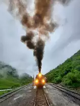 Bei trübem Wetter hat die Lok 704 des Dampfzuges von Realp nach Oberwald in der Station Tiefenbach Wasser gefasst. Die nasse Witterung hat die Fahrgäste davon abgehalten, das Prozedere live mitzuverfolgen. Während des Aufenthaltes des Zuges ist es erlaubt, sich auf den Gleisen aufzuhalten. In diesem Fall übt der Fotograf auch die Funktion des Zugchefs aus, das heisst, ohne dessen Erlaubnis bewegt sich kein Fahrzeug. Tiefenbach, 8.7.2021