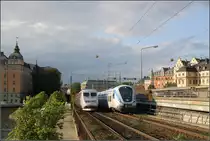 Im Herzen Stockholms - 

Begegnung eines X 60-Pendeltågzugs mit einem X 2000-Fernverkehrstriebzug. Der gesamte Bahnverkehr einschließlich der Güterzüge muss südlich von Stockholm C auf nur zwei Gleisen abgewickelt werden. Die Zugfolge ist entsprechend hoch. Erst ab Stockholm Södra stehen vier Gleise zu Verfügung und der Pendeltågverkehr fährt auf seinen eigenen Gleisen. Im Innenstadtbereich wird deshalb zu Entschärfung der Situation die sogenannte Citybanan gebaut werden, eine unterirdische Pendeltåg-Strecke von der Station Karlsberg bis kurz vor die bestehende Tunnelstation Södra. Es wird zwei unterirdische Bahnhöfe geben, Odenplan und City (unter dem Bahnhof T-Centralen der U-Bahn). Auch an der Station Odenplan kann zur U-Bahn umgestiegen werden. Die Strecke wird teilweise in bis zu 40 Meter Tiefe liegen. Im Bereich zwischen Riddarholmen und Södermal wird der Tunnel auf den Seeboden des Riddarfjörden aufgesetzt. Man fährt dann quasi durch das Wasser. 

19.8.02007 (M)