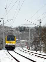 Um 11.08 am 25.03.08 hatte das Schneegest�ber aufgeh�rt und die Sonne zeigte sich sogar, als E-Lok 3010 mit ihren schneebedeckten Wagen aus Richtung Clervaux durch die Kurve vor Enscherange f�hrt.