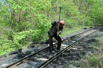 Gekonnt h�mmert der Bahnarbeiter die N�gel in die Schwellen. Vor ihm sieht man das Spurmass! Die Schwellen sind aus unbehandeltem Birkenholz tw mit Rinde. Das  Schotterbett  ist Dreck und Schlacke!