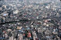 Serie 103: Beim scharfen Hinsehen erkennt man einen hellgrünen 10-Wagenzug der Ringlinie (Yamanote-Linie) zwischen Tokyo-Ikebukuro und Tokyo-Ôtsuka. Aufnahme vom Sunshine-Building in Ikebukuro, 17.Juli 1979. Heute ist die Dachlandschaft unruhiger, mit viel mehr höheren Häusern. YAMANOTE-LINIE 