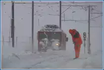 Gem 4/4 801 macht sich aus dem Staub, w�hrend der Arbeiter versucht mit einem Pickel den festgepressten Schnee, der hart wie Beton ist, aus einer Weiche zu entfernen. (01.12.2009)