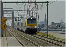 Diese eigenwillige Zugkomposition (composition dromadaire) verbindet st�ndlich Antwerpen Centraal mit dem Bahnhof Noorderkempen, welcher an der Hochgeschwindigkeitsstrecke L 4 in der N�he der niederl�ndischen Grenze liegt. Da die Loks der S�rie 13 noch nicht mit dem Sicherheitssystem ETCS ausgestattet sind, die M 6 Steuerwagen dieses System aber schon besitzen, f�hrt die Lok (hier 1350) in der Mitte des Zuges. Das Bild wurde am 23.06.10 in Antwerpen Luchtbal aufgenommen und am rechten Bildrand ist die  Kathedrale der Eisenbahn  Antwerpen Centraal zu sehen. (Jeanny)