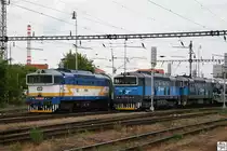 754 057-8 zieht am 7. Juni 2012 einen Personenzug an den mit einem Autotransport-Zug wartenden 753 769-9 und 753 770-7 im Bahnhof Plzeň (Pilsen) vorbei.