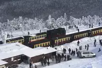 Bahnhof Brocken am Nachmittag des 26.01.2013. Diese Aufnahme erfolgte per Zoom durch die Scheibe von der Aussichtsplattform des Brockenturms aus. Der vordere Zug (auf Gleis 1) ist Planzug P8922, welcher gleich nach Drei Annen Hohne fahren wird. Direkt dahinter, auf Gleis 3, steht  Sonderzug  Quedlinburger Brockenexpress  mit Zuglok 99 7245 bereit, der einige Zeit sp�ter nach Wernigerode startet. Von dem Kleinbus am Bahnhof sollte man sich nicht t�uschen lassen. Dieser geh�rt dem Brockenwirt. Es ist nur einigen wenigen Fahrzeugen mit Sondergenehmigung gestattet, auf den Brocken zu fahren! Der �ffentliche Verkehr endet in Schierke. Sp�testens hier mu� man seinen Privat-PKW abstellen und den Rest der Strecke zu Fu�, oder mit einem Zug der HSB bew�ltigen.