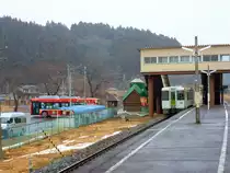 Hier in Yanaizu endet heute die Kesennuma-Linie; links ist der Bahnersatz-Bus (von JR Ost-Japan betrieben) zu sehen, der die Fahrgäste weiter in die Katastrophengebiete bringt. Der Bus ist in fröhlichem Leuchtendrot gestrichen und mit Bildern der verschiedenen Maskottchen und Figürchen versehen, welche die Stationen der Kesennuma-Linie markiert haben. Im Bahnhof steht der einzelne Triebwagen (KIHA 110-125), der das Reststück der Bahnlinie bedient; 15.Februar 2013. 