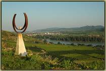 Blick von den Weinbergen in die Wachau. Im Hintergrund ist Stift G�ttweig zu sehen, und wenn man genau hin sieht, sieht man auch einen 5047 im neuen CS Design als Regionalzug von Krems nach Spitz an der Donau. Am  H�henweg , den wir entlang gewandert sind, befinden sich eine Menge Kunstobjekte, wie links im Bild eines zu sehen ist. Die Aufnahme entstand am 24.9.2006.