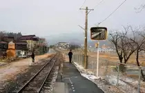 Ôfunato-Linie, Bahnhof Shishiori Karakuwa am 20.Februar 2013: Der Tsunami vom 11.März 2011 hat die ganze Ortschaft hinweggespült; nach dem Einsturz von Oeltanks am Hafen hatte sich der Tsunami als brennende Walze über Shishiori Karakuwa ergossen. Im Hintergrund rechts stehen ein paar Baracken für die Nothilfe. Im Spiegel wird sich der Triebwagen vom oberen Bild nie mehr spiegeln. 
