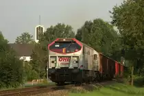 Schwerer Güterverkehr auf der Werkbahn nach Georgsmarienhütte. Am 28.7.2014 war wieder der OHE Tiger 330094 mit einem langen Schrottzug unterwegs. Hier fährt der Zug um 8.51 Uhr gerade in die lange Steigung am ehemaligen Bahnhof Wulfskotten. Im Hintergrund ragt noch der Turm der St. Josef Kirche über die Bäume heraus.