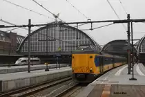 Ein Koploper der NS wartet ebenso wie im Hintergrund ein ICE 3 am 27.10.2014 auf 
Ausfahrt in Amsterdam Centraal. Über allem schmückt das Flügelrad die große Bahnhofshalle.