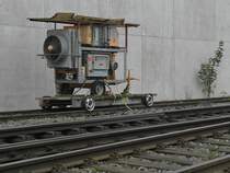 Man nehme 4 Pkw-Felgen, 2 Rohre, 2 Balken, einige Bretter, verbinde diese Teile und fertig ist ein Fahrgestell für ein Gleis. Gesehen in Altshausen an der Rückseite eines Lagerhauses am 11.10.2014. Aufnahmestandort ist die Böschung am Bahnübergang beim Bahnhof.