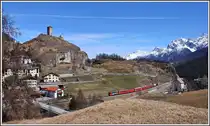 RE1244 von Scuol-Tarasp nach Disentis/Mustér erreicht Ardez. Mit dreieinhalb Stunden ist es neben dem Berninaexpress der längste durchgehende Zuglauf der RhB. Zuglok ist die Ge 4/4 II 615  Klosters . Auf dem Hügel thront die Ruine Steinsberg und am Dorfrand steht die Katholische Kirche. (09.04.2015)