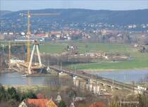 W�hrend eine  Kn�delpresse  (BR 180) in Farbgebung DR auf der Br�cke die Elbe �berquert, schiebt sich ein Frachtkahn an der Baustelle f�r die neue Stra�enbr�cke vorbei - Niederwartha, 09.03.2007
