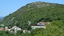 1141 019 schraubt sich mit einer Reihe Eoas als Tv 61005 Rijeka - Zagreb Ranžirni kolodvor am 10.07.2015 die Rijekarampe hoch. Hier passiert sie gerade die Ortschaft Draga