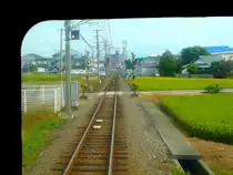 Iyo-Bahn, Gunchû-Linie: Blick auf die bevorstehende Kreuzung mit einem Gegenzug in Okada. Bunt zusammengewürfelte Landschaft mit eher städtischen Bauten, Bauernhäusern und überall kleinen Reisfeldern. 18.September 2009. 
