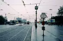 Wien am 31. Oktober 1976: Straßenbahnhaltestelle Mexikoplatz für stadtauswärts fahrende Züge der Linien B, BK, 25 und 26. In der Haltestelle für die stadteinwärts fahrende Züge der selben Linien hält eine E1+c2/c3-Garnitur, die kurz vorher über die Notbrücke, die in kurzer Zeit als Ersatz für die am 1. August 1976 eingestürzte Reichsbrücke errichtet worden war, gefahren war. - Am Ende der Straße stehen einige Leute, die an die Reste der eingestürzten Reichsbrücke schauen. - Scan von einem Diapositiv. Film: Agfachrome 50. Kamera: Leica CL. 