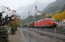 Bei strömendem Regen fährt die 185 100-5 mit einem Güterzug bei Flüelen dem Gotthard entgegen. Auf dem kleinen Hügel oberhalb thront die katholische Kirche von Flüelen. 14.10.2016