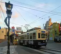 Die Strassenbahn von Nagasaki: Nagasaki war im streng abgeriegelten Japan während über 220 Jahren die einzige Schnittstelle mit dem Ausland, wobei von den westlichen Kulturen allein die Holländer auf einer Insel in der Bucht eine kleine Niederlassung betreiben durften (für den Import von technologischem Wissen wie Optik oder Dammbau nach Japan und den Export etwa von Porzellan aus Japan). Daneben unterhielt China eine Niederlassung in Nagasaki, durch die viele chinesische Traditionen Japan erreichten; ein gewisses chinesisches Flair ist an dem Lampenmast mit seinem chinesischen Drachen zu sehen. Aufnahme des Wagens 377 an der Endstation des mittleren Zweigs der Strassenbahn an die Berge im Osten. 8.August 2013.  